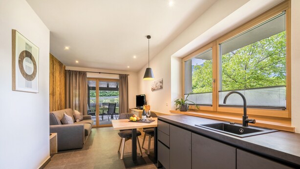 A modern kitchen with a large window, a dining area with a table and chairs, and a sofa in the adjacent living area.