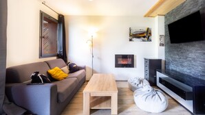 Una sala de estar moderna con un sofá, una mesa de centro de madera, una chimenea y un televisor de pantalla plana montado sobre una pared de piedra.