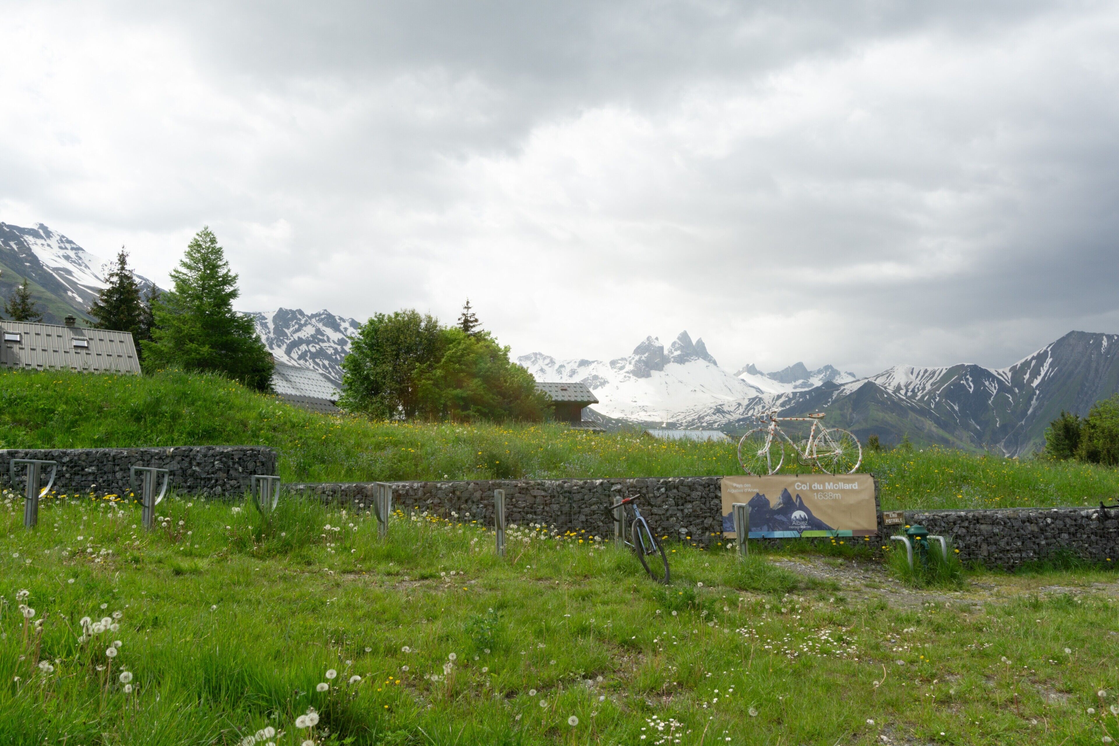 A grassy field with a stone wall, a bicycle, and a sign indicating a mountain peak at 1633m.