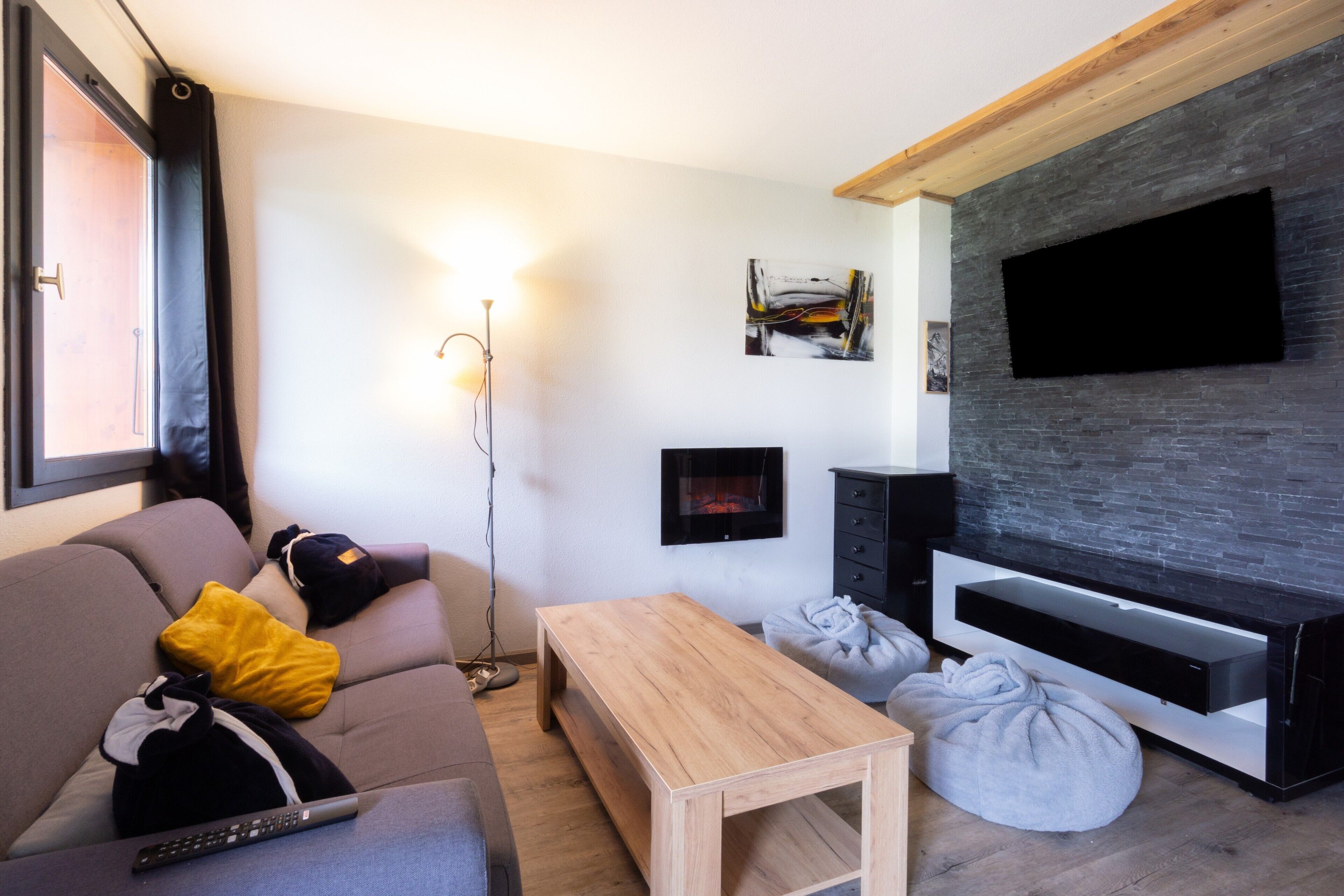 A modern living room with a sofa, a coffee table, a TV on a stone wall, and a floor lamp.
