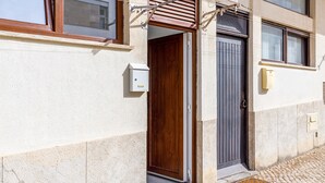 Ein Gebäudeeingang mit einer Holztür, einem Metallgitter und einer kleinen Stromklemme an der Wand.