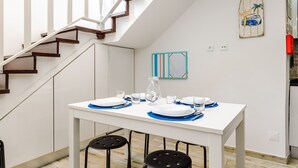 Ein Essbereich mit einem weißen Tisch, gedeckt für vier Personen, eine Treppe und ein Küchenbereich im Hintergrund.