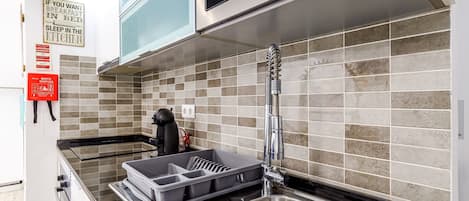 A modern kitchen with a stainless steel sink, a kettle, and a tray with utensils.