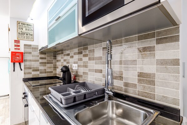 A modern kitchen with a stainless steel sink, a kettle, and a tray with utensils.