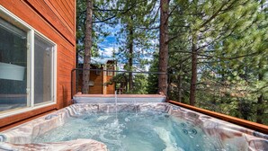 Un jacuzzi con interior de mármol, rodeado de árboles y una terraza de madera.