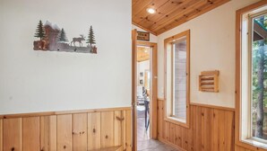 Un intérieur en bois avec un banc, un mur en bois orné d’une œuvre d’art sur le thème de la nature, et une fenêtre donnant sur des arbres.