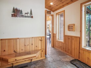 A wooden interior with a bench, a wooden wall with a nature-themed artwork, and a window with a view of trees. - Bear Peak by Tahoe Getaways - 3BR Pet-Friendly w Hot Tub, EV Charger & HOA (Truckee)