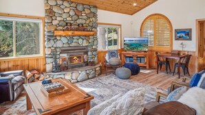 Un salón acogedor con chimenea de piedra, techo de madera y un ventanal grande con vistas panorámicas.