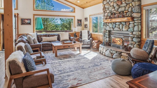 Una sala de estar acogedora con chimenea de piedra, techo de madera y ventanas amplias que ofrecen vistas al exterior.