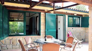 An outdoor patio with wicker chairs, a table set for dining, and a stone wall with green shutters. - Holiday apartment mit Pool (Guardistallo)