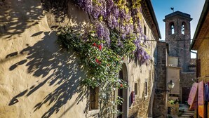 A narrow street with a building featuring a hanging flower basket and a bell tower in the background. - Holiday apartment mit Pool (Guardistallo)