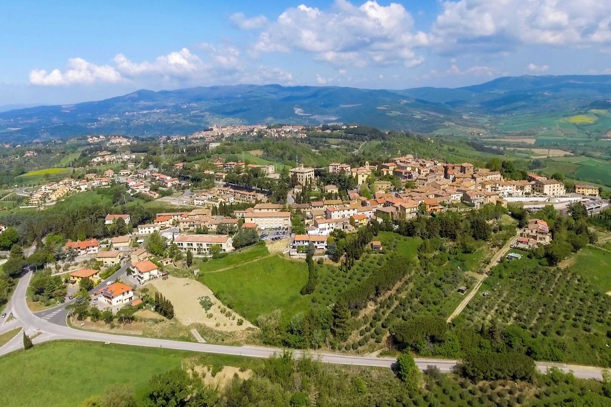 An aerial view of a town with a central cluster of buildings, surrounded by green fields and hills.
