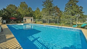 Ein rechteckiger Swimmingpool mit blauer Liegefläche, umgeben von einem Zaun und Bäumen.