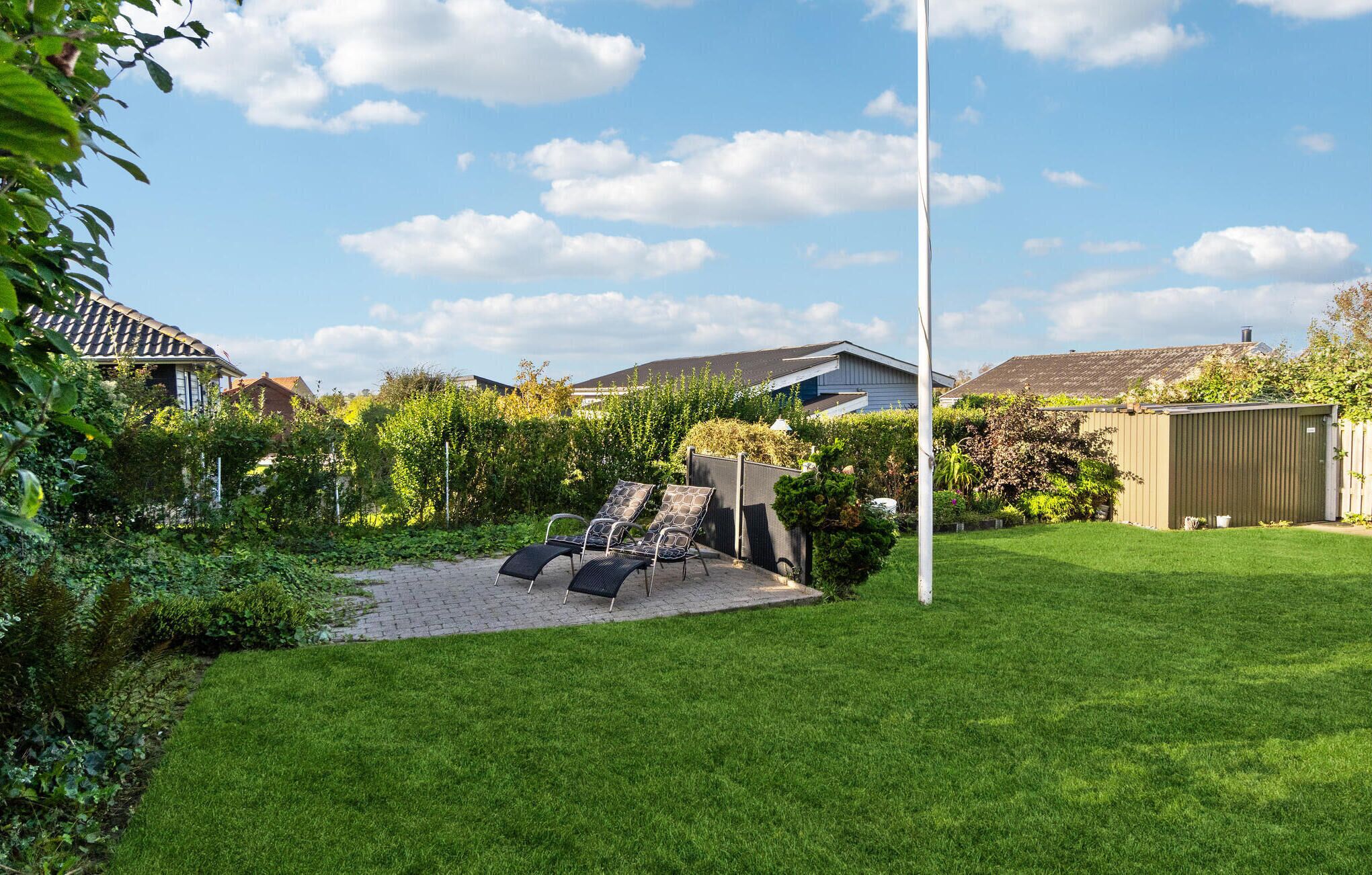 A backyard with a paved patio, two lounge chairs, a tall white pole, and a green lawn.