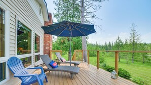 Eine Holzterrasse mit zwei Liegestühlen und einem blauen Sonnenschirm mit Blick auf eine grüne Landschaft.