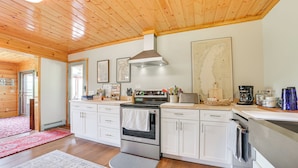 Una cucina moderna con soffitto in legno, elettrodomestici in acciaio inox, mobili bianchi e un tappeto rosso.