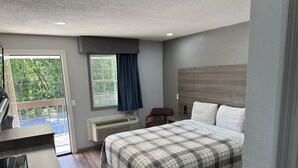 A bedroom with a bed, a desk, a chair, a window with curtains, and a view of greenery outside. - Budget Inn Express (Columbia)