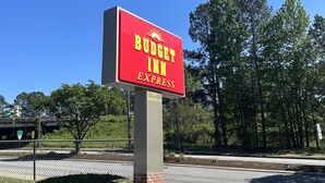 A red sign for Budget Inn Express with a clear view of the surrounding area including trees and a road. - Budget Inn Express (Columbia)