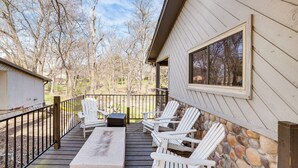 Una terraza con sillas Adirondack blancas, un muro de piedra y una ventana con vistas a un área boscosa.