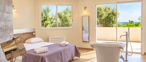 Un dormitorio con cama, un baño con bañera, un ventanal grande y vistas a zonas verdes.