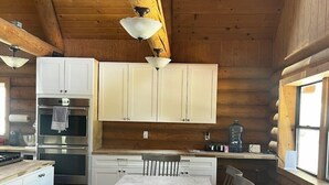 Une cuisine rustique aménagée dans une cabane en rondins, avec des meubles blancs, une table à manger en bois et un banc.