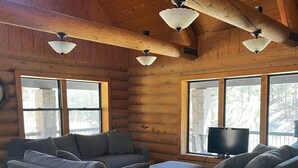 L’intérieur d’une cabane en rondins, avec un ensemble de canapés, un téléviseur et de grandes fenêtres.