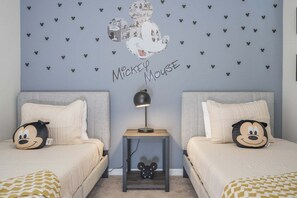 Een tweepersoonskamer met twee bedden, elk voorzien van een Mickey Mouse kussen, een nachtkastje met lamp en een muur versierd met Mickey Mouse stickers.