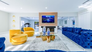 A modern living room with a large TV, blue sofas, and yellow chairs. - Encanto Luxury Home (Miami)