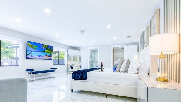 A modern bedroom with a large bed, a bench, a painting, and a lamp. - Encanto Luxury Home (Miami)