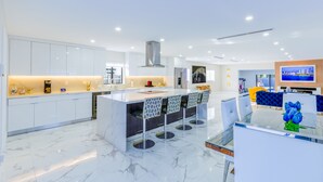 A modern kitchen with white cabinets, a marble countertop, and a central island with bar stools. - Encanto Luxury Home (Miami)