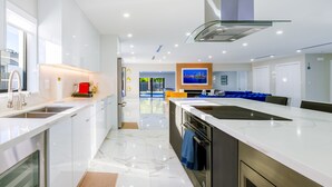 A modern kitchen with white cabinetry, a large island, and a built-in oven. - Encanto Luxury Home (Miami)