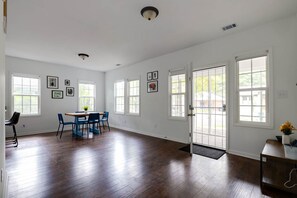 Una habitación amplia con pisos de madera, una zona de comedor con sillas azules y varios ventanales que dejan entrar luz natural.