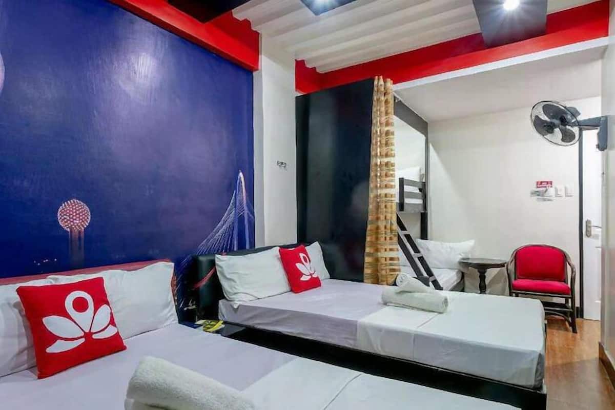 A hotel room with two beds, a red chair, a fan, and a mural on the wall.