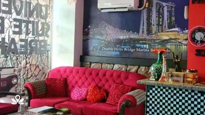 A red sofa with multiple cushions, a wall-mounted air conditioner, a poster of the Double Helix Bridge Marina, and a clock on the wall. - Sabel Travelers Inn (Laoag)