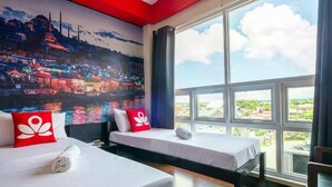 A hotel room with two beds, a large window with a view of the city, and a mural of a cityscape on the wall. - Sabel Travelers Inn (Laoag)