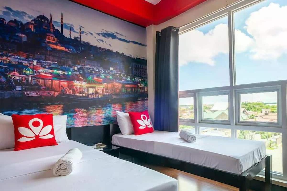A hotel room with two beds, a large window with a view of the city, and a mural of a cityscape on the wall.