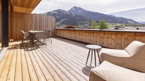 Um deck de madeira com mesa e cadeiras, com vista para uma paisagem montanhosa.