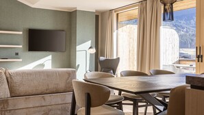 Uma sala de estar moderna com sofá, mesa de jantar, cadeiras, televisão de tela plana e uma grande janela com cortinas.
