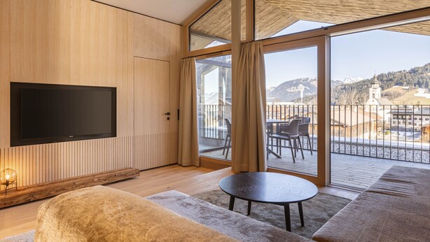 Ein modernes Wohnzimmer mit großem Fernseher, einer gemütlichen Couch, einem kleinen Tisch und einem Balkon mit schöner Aussicht.