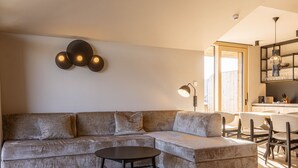 Ein modernes Wohnzimmer mit einer Eckcouch, einem runden Couchtisch und einem Essbereich mit Stühlen sowie einer Küche im Hintergrund.