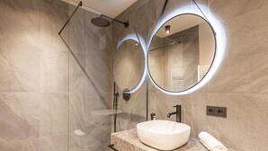 A modern bathroom with a glass-enclosed shower, a large oval mirror, and a marble sink. - Premium mit 2 Schlafzimmer by Interhome (Oberndorf in Tirol)