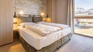 A modern bedroom with a large bed, wooden headboard, and a view of mountains through a large window. - Premium mit 2 Schlafzimmer by Interhome (Oberndorf in Tirol)