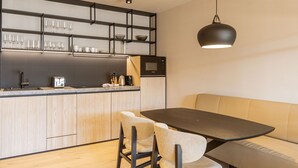 A modern kitchen with a built-in microwave, a coffee maker, and a kettle on the counter. There is a dining table with chairs and a bench.