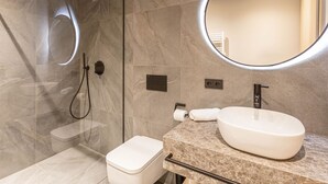 A modern bathroom with a glass-enclosed shower, a large oval sink, and a round mirror.