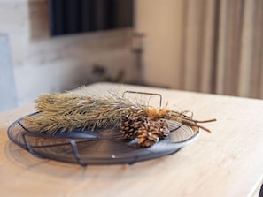 A clear glass bowl on a wooden table with pine branches and pine cones.