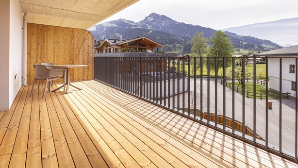 A wooden deck with a table and chairs, overlooking a mountain landscape with buildings.