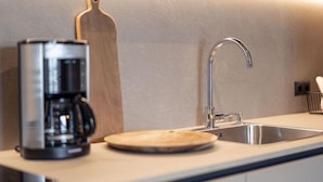 A modern kitchen with a coffee maker, a wooden cutting board, and a stainless steel sink.