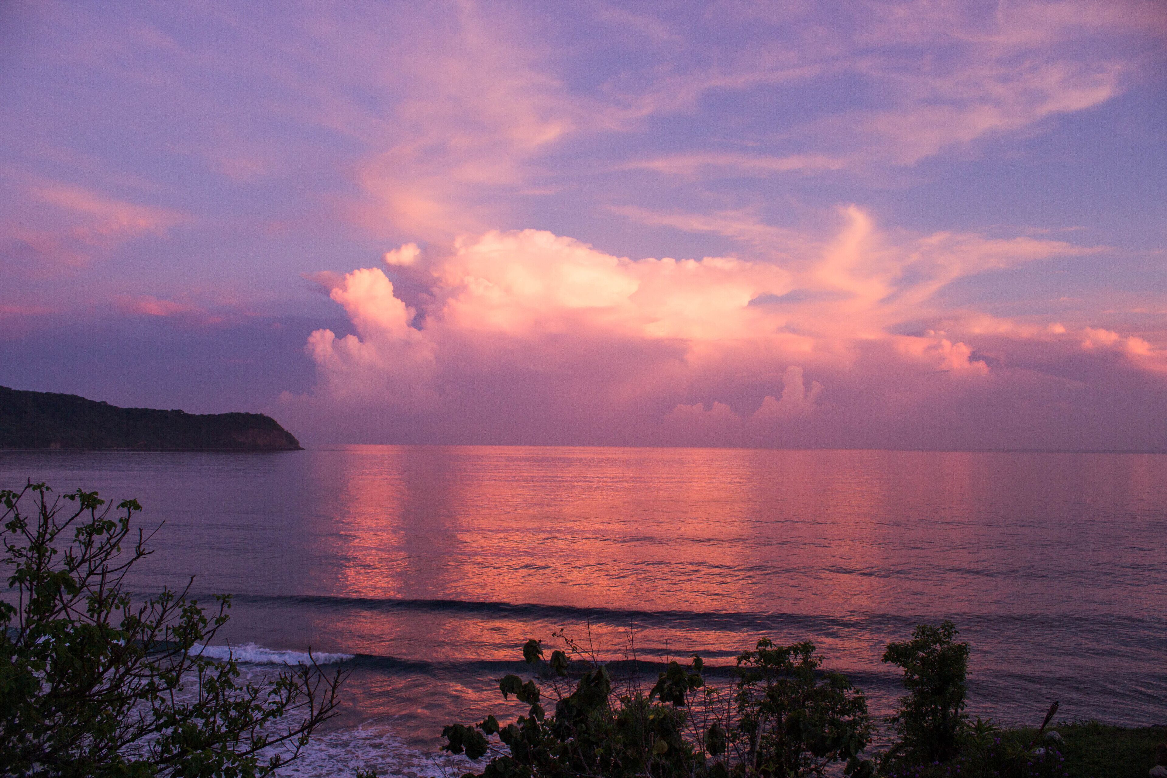 Un atardecer costero con mar en calma y tierra a lo lejos.