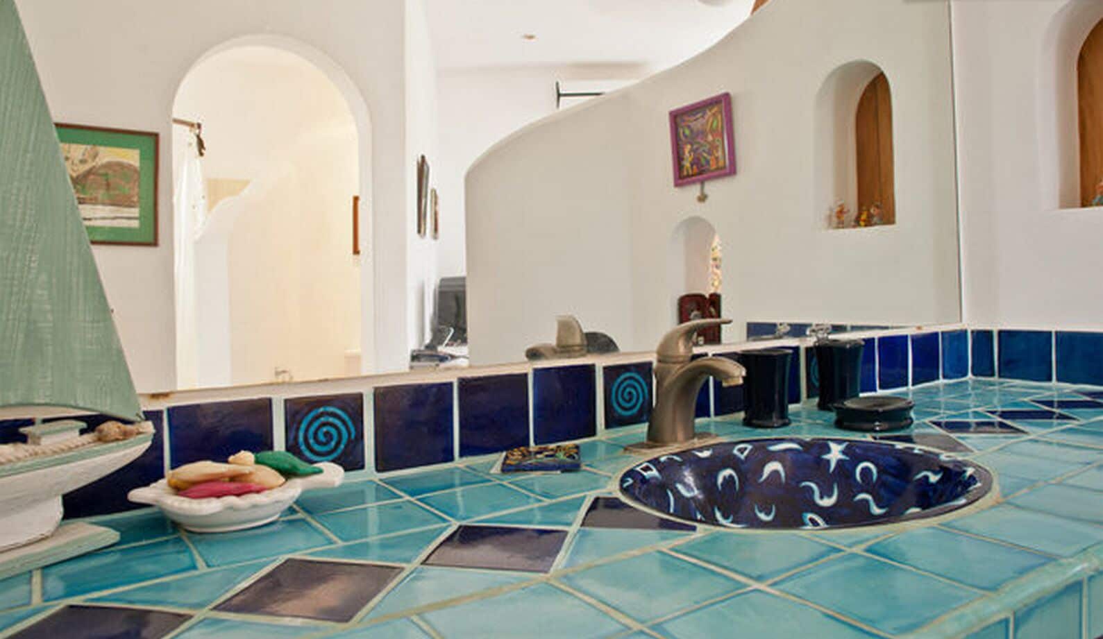 Ein Badezimmer mit blau-weißen Fliesen, einem Waschbecken mit einer verzierten Schüssel und einem Spiegel darüber.