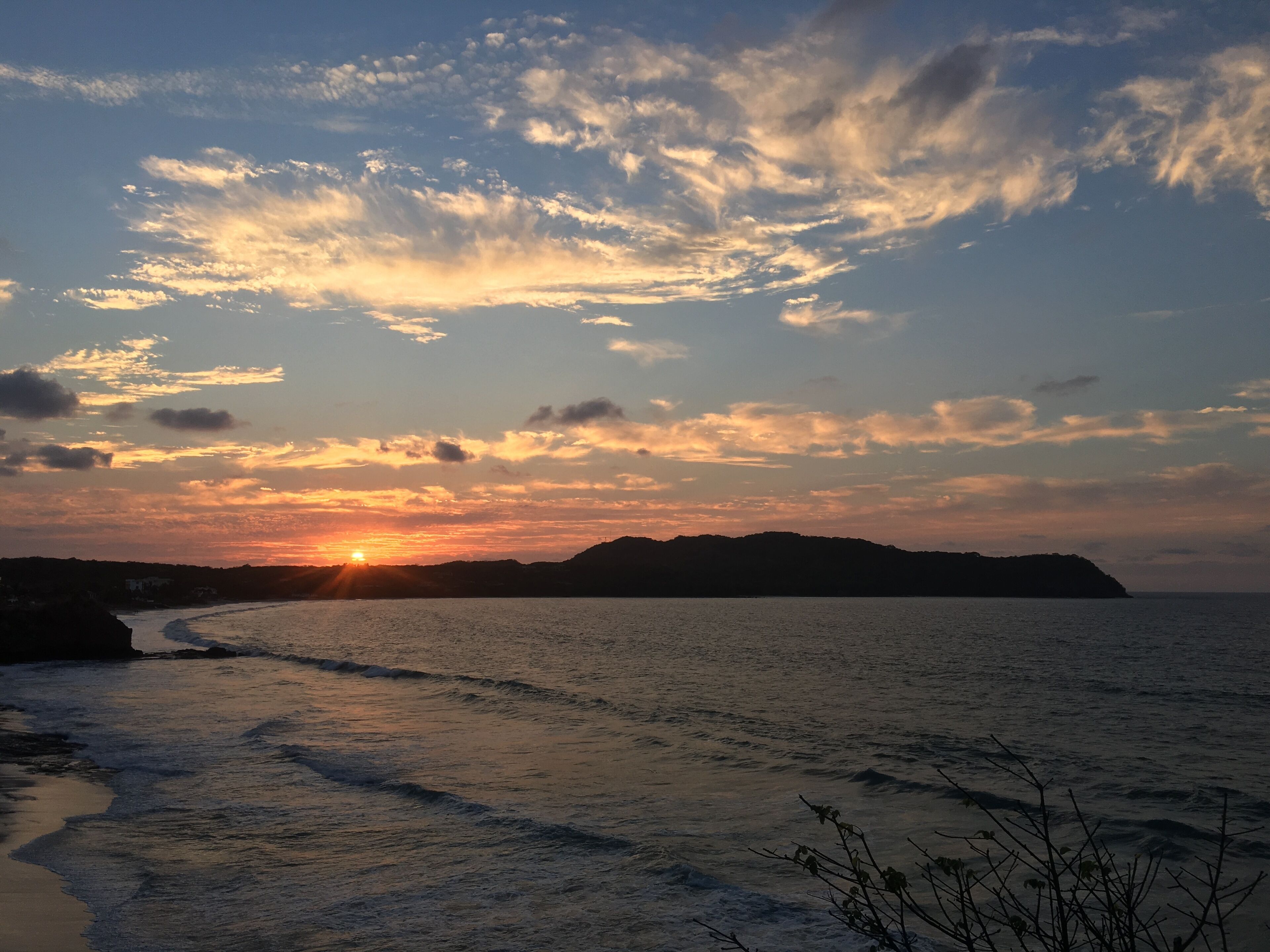 Solnedgang over et kystlandskab med bølger, der nærmer sig stranden.